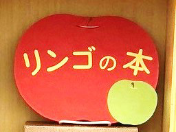 小展示「リンゴの本」の看板の写真。大きな赤いリンゴの形をした看板に、展示タイトル「リンゴと本」が書かれ、右下に小さな青リンゴが貼り付けられている。